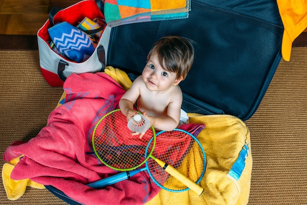 Bambina sorridente seduta dentro una valigia pronta per andare in vacanza