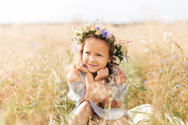 Bambina sorridente sveglia con la corona di fiori sul prato. Ritratto di bambino adorabile all'aperto.