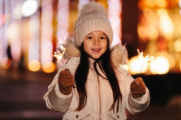 Bambina sorridente sveglia con luci del Bengala sulla strada la sera in inverno