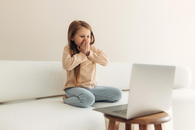 Bambina spaventata che chiude il viso con le mani che guardano lo schermo del laptop