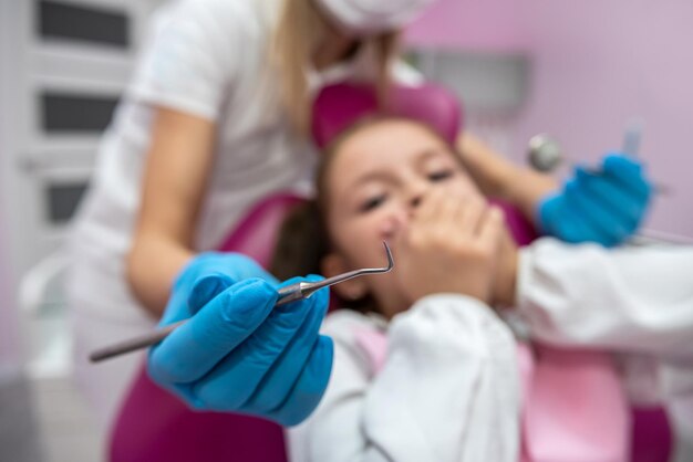 Bambina spaventata che si copre la bocca con le mani mentre visita il dentista Primo piano di un ortodontista che cerca di controllare i denti di un bambino spaventato seduto su una poltrona odontoiatrica in una clinica
