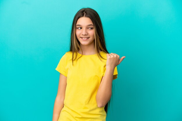 Bambina su sfondo blu isolato che punta al lato per presentare un prodotto