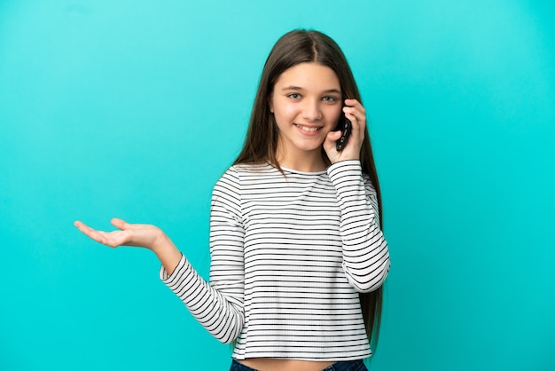 Bambina su sfondo blu isolato mantenendo una conversazione con il telefono cellulare con qualcuno