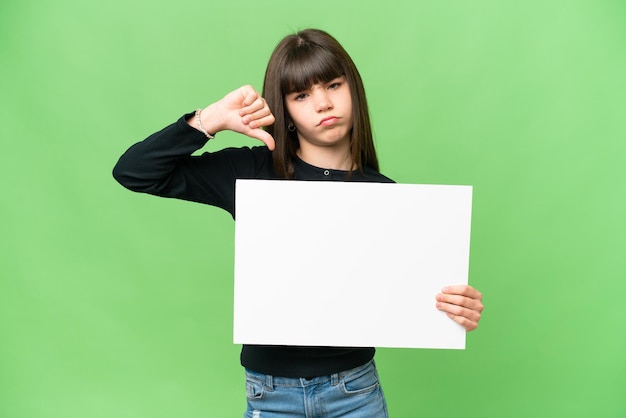 Bambina su sfondo chroma key isolato che tiene un cartello vuoto e fa un cattivo segnale