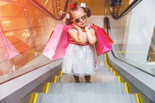 Bambina sulla scala mobile nel centro commerciale con gli acquisti