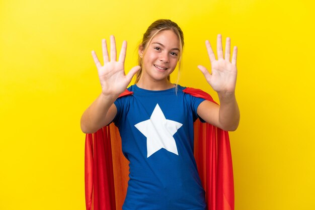 Bambina Super Hero isolata su sfondo giallo che conta dieci con le dita