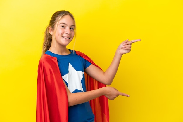 Bambina Super Hero isolata su sfondo giallo che punta il dito di lato e presenta un prodotto