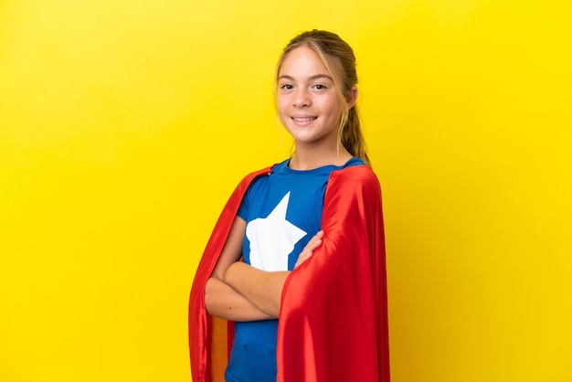 Bambina Super Hero isolata su sfondo giallo con le braccia incrociate e guardando avanti