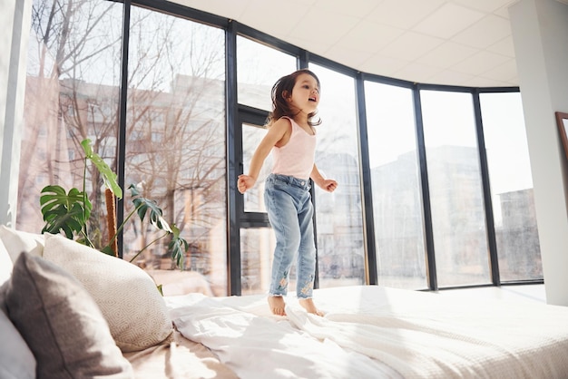 Bambina sveglia a casa da sola Divertirsi saltando sul letto