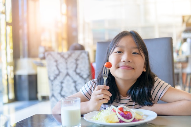 Bambina sveglia asiatica che mangia pomodoro fresco e insalata la mattina. Sano e rilassarsi sul concetto di vacanza