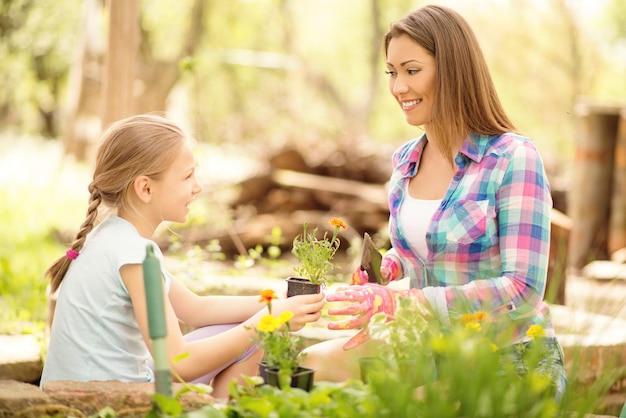 Bambina sveglia che aiuta sua madre a piantare fiori in un cortile.