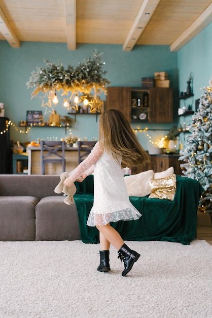 Bambina sveglia che balla vicino all'albero di Natale. La gioia dei bambini Nelle vacanze di Capodanno