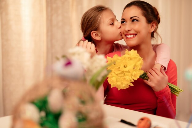 Bambina sveglia che dà a sua madre i narcisi gialli del mazzo e ti bacia.