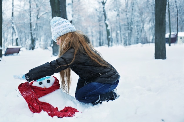 Bambina sveglia che fa pupazzo di neve nel parco invernale