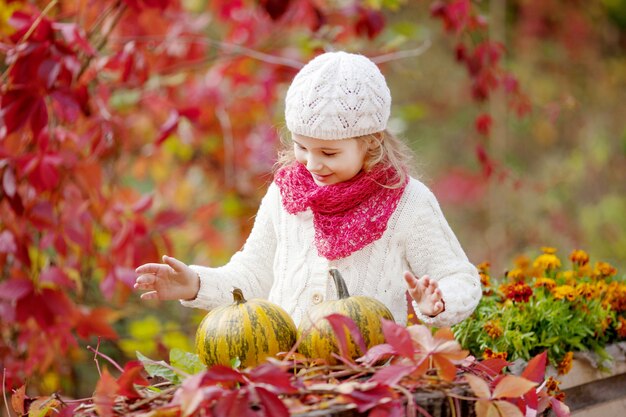 Bambina sveglia che gioca con le zucche nel parco di autunno. Attività autunnali per bambini