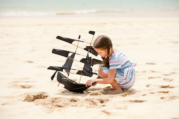 Bambina sveglia che gioca sull'aquilone della nave volante della spiaggia