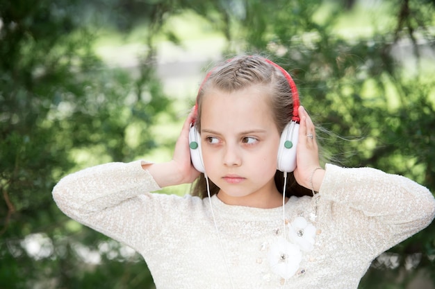 Bambina sveglia che gode della musica usando le cuffie al giorno d'estate