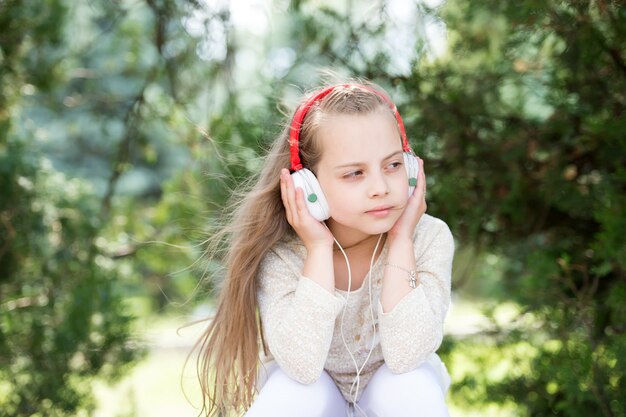 Bambina sveglia che gode della musica usando le cuffie al giorno d'estate