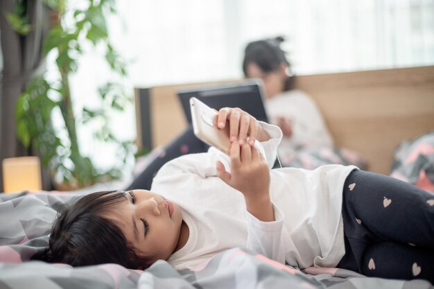 Bambina sveglia che guarda video sullo smartphone con la faccina sorridente da sola sul letto bambino che usa il telefono cellulare con la faccia felice a casa Resta a casa quarantena coronavirus COVID19 prevenzione della pandemia