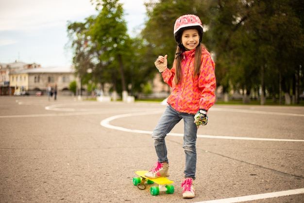 Bambina sveglia che indossa il casco cavalcando uno skateboard nel bellissimo parco estivo