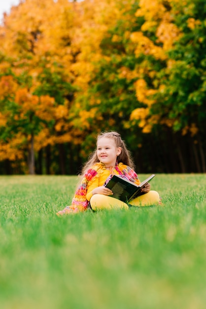 Bambina sveglia che legge un libro nel parco d'autunno