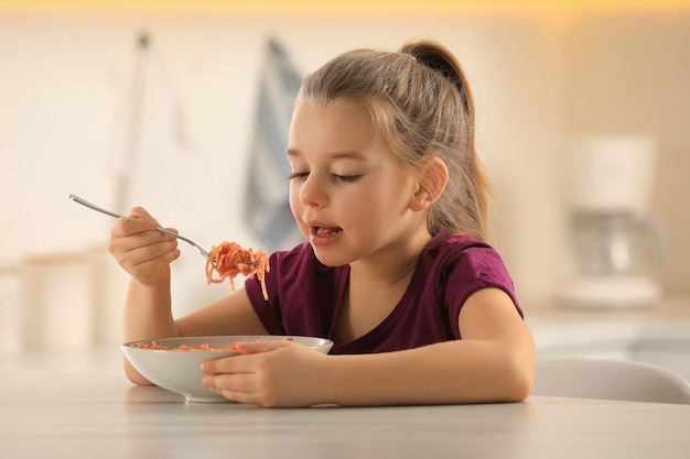 Bambina sveglia che mangia pasta saporita alla tavola in cucina