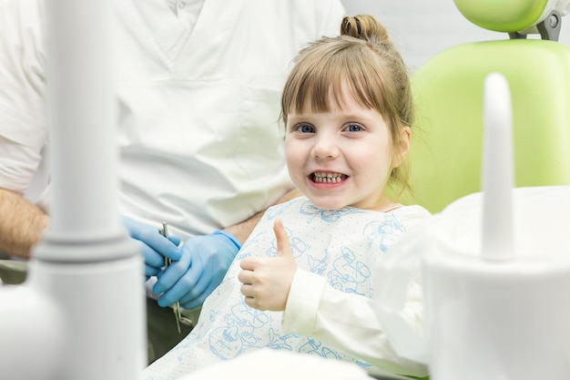 Bambina sveglia che mostra il pollice sul segno alla clinica dell'ufficio del dentista