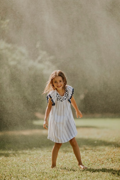 Bambina sveglia che si diverte con l'acqua sotto l'irrigatore di irrigazione