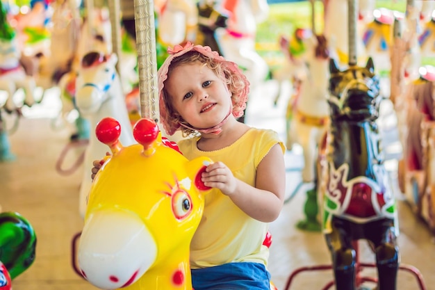 Bambina sveglia che si diverte nel luna park e che cavalca su una giostra colorata.