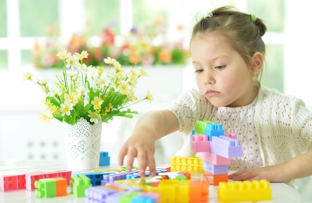 Bambina sveglia che si siede al tavolo e che raccoglie blocchi di plastica colorati