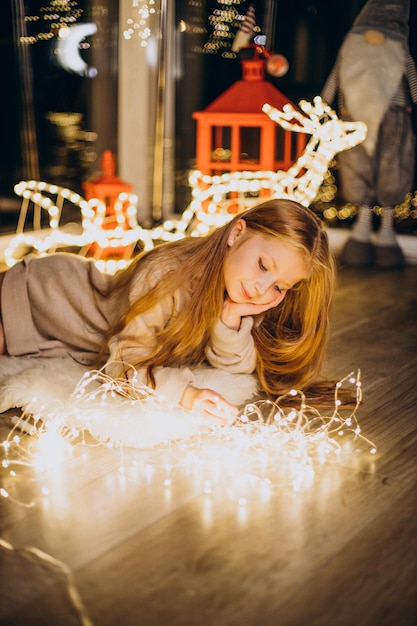 Bambina sveglia che si siede dalle luci di Natale alla vigilia