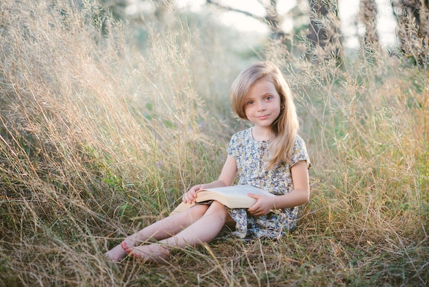 Bambina sveglia che si siede sull'erba e che legge un libro nel