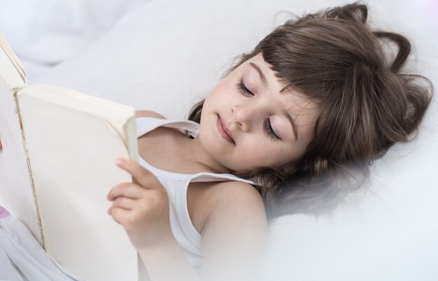 Bambina sveglia che sorride mentre giaceva in un accogliente letto bianco
