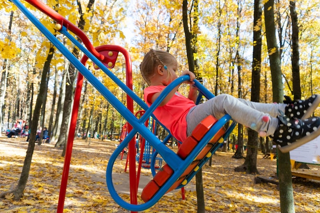 Bambina sveglia che sorride mentre oscilla sull'altalena nel parco di autunno