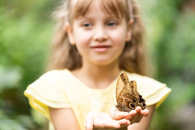 Bambina sveglia che tiene bella farfalla vivente sulla sua mano