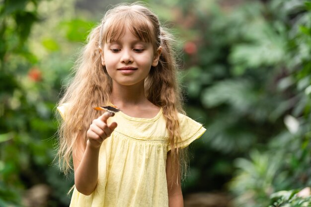 Bambina sveglia che tiene bella farfalla vivente sulla sua mano