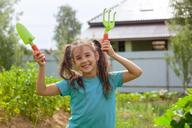 Bambina sveglia che tiene piccoli attrezzi da giardinaggio che ballano nel giardino