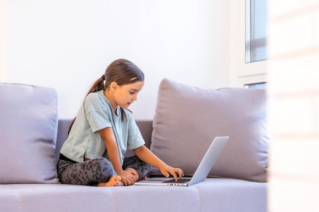 Bambina sveglia che utilizza il computer portatile a casa. Istruzione, studio online, studio a casa, apprendimento a distanza, concetto di stile di vita dei bambini delle scolarette