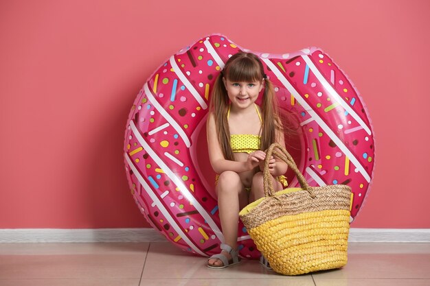 Bambina sveglia con anello gonfiabile e borsa da spiaggia vicino alla parete colorata