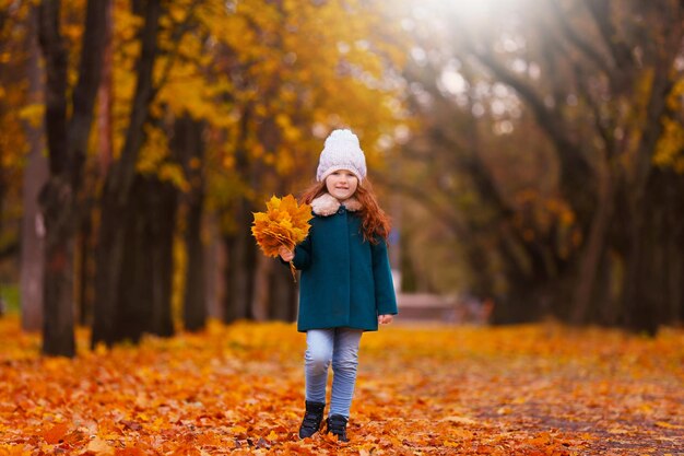 Bambina sveglia con bouquet di foglie gialle nel parco autunnale