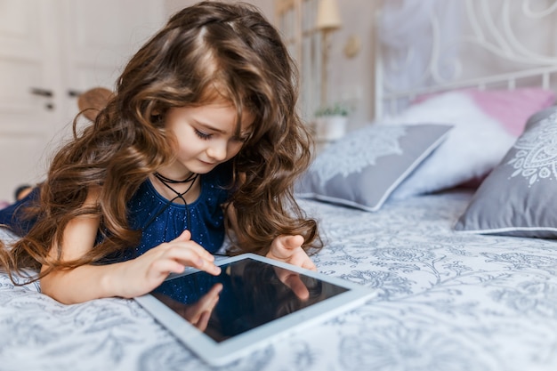 Bambina sveglia con capelli ricci utilizzando la tavoletta digitale