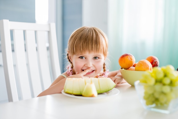 Bambina sveglia con i frutti sul tavolo