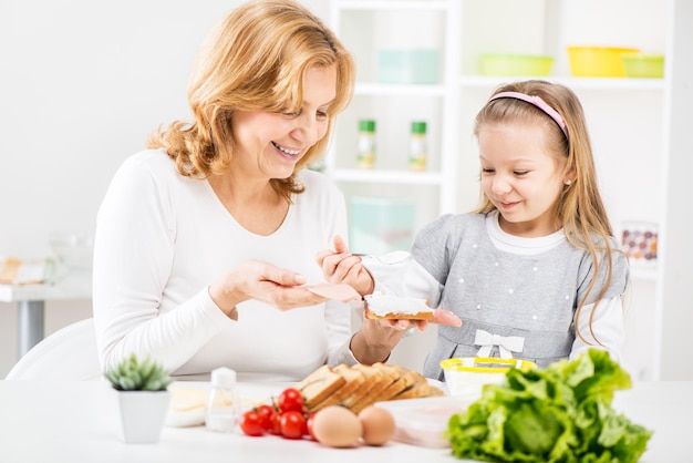 Bambina sveglia con la bella nonna che fa un panino in cucina.