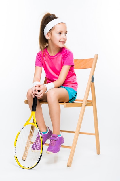 Bambina sveglia con la racchetta di tennis in sue mani su bianco
