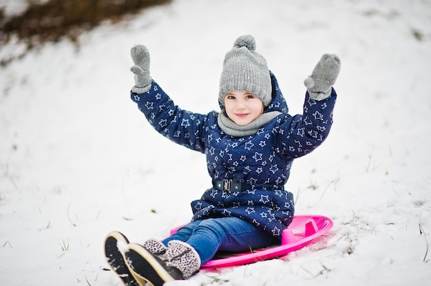 Bambina sveglia con le slitte del piattino all'aperto il giorno di inverno.