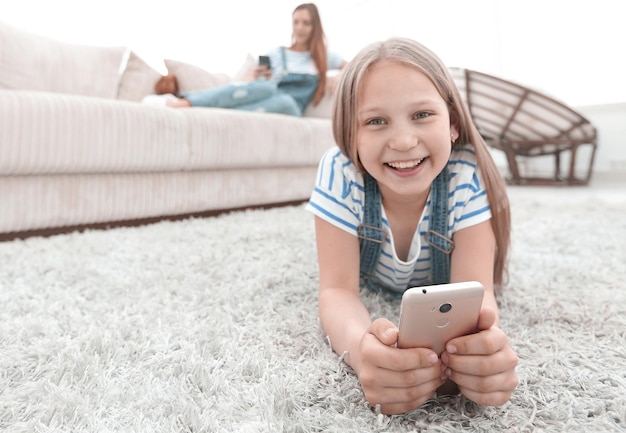 Bambina sveglia con lo smartphone sdraiato sul tappeto nel soggiorno