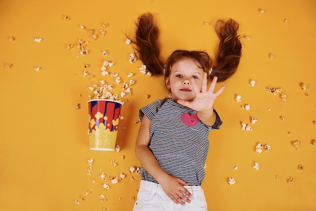 Bambina sveglia con popcorn sdraiato sul pavimento giallo.