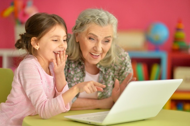 Bambina sveglia con sua nonna che utilizza un computer portatile moderno