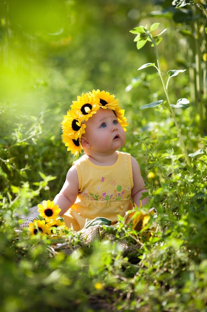 Bambina sveglia con una corona di girasole seduta sul campo di girasoli e ha studiato la natura intorno