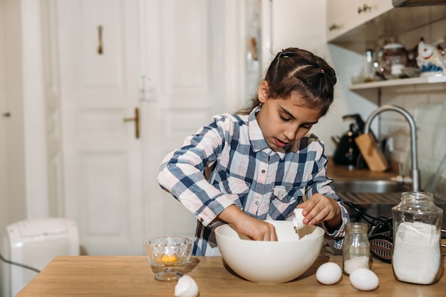 Bambina sveglia divertente che prepara la pasta in cucina. Il bambino cuoce i biscotti in cucina a casa.